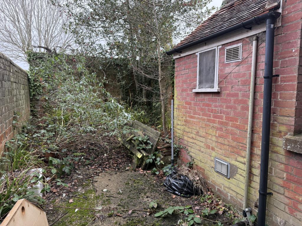 Lot: 88 - FREEHOLD COMMERCIAL PROPERTY ON HIGH STREET - Garden with overgrowth and concrete patio area
